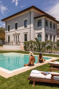 two people sitting by a swimming pool in front of a house at Livia Valeria Palace in Rome