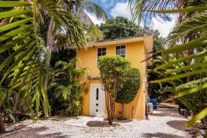 a yellow house with a white door and some palm trees at Appartement met zwembad en prachtige tuin in Willemstad