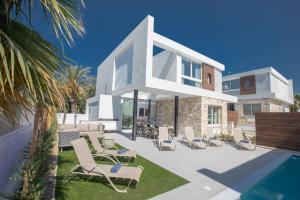 a white house with chairs and a swimming pool at Kube Luxury Villas in Ayia Napa