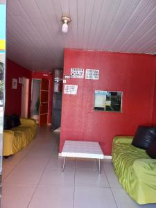 Habitación con 2 camas y un banco contra una pared roja. en Pousada Kaka en Teresina