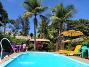 - une piscine avec des chaises, un parasol et des palmiers dans l'établissement Pousada Canto De Imbassai, à Imbassaí