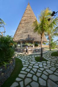 Un uomo che cammina davanti a un tavolo con una capanna di paglia di Sudamala Resort, Komodo, Labuan Bajo a Labuan Bajo