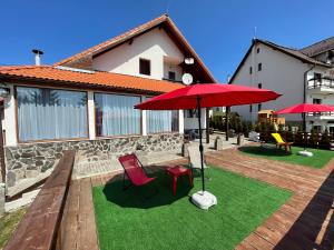 un patio con due sedie e un ombrellone rosso di Red Family Apartments a Păltiniş