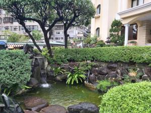a pond in a garden with a waterfall and trees at Beautyage Spring Hotel in Taipei