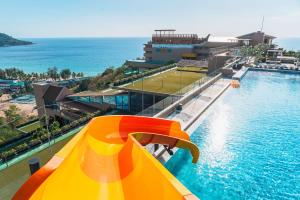 a swimming pool with an orange and yellow slide next to the ocean at The Sea Galleri by Katathani - SHA Plus in Kata Beach