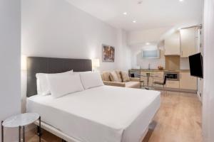 a bedroom with a large white bed and a kitchen at Apartamentos Metrópolis in Seville