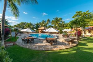 een buitenzwembad met tafels, stoelen en parasols bij Hotel Pousada Imbassai in Imbassai