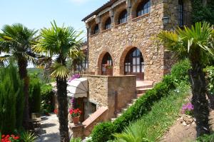 una casa de piedra con palmeras delante en Hotel Galena Mas Comangau en Begur