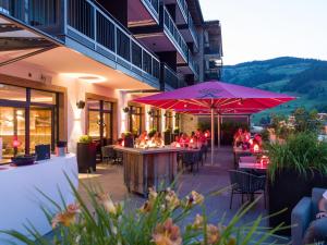 un restaurant avec des tables, des chaises et un parasol rose dans l'établissement Hotel Adapura Wagrain, à Wagrain
