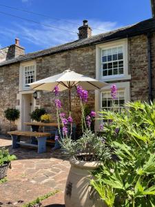 a house with an umbrella and a bench and flowers at The Cosy Nook Cottage Company - Cosy Cottage in Warcop