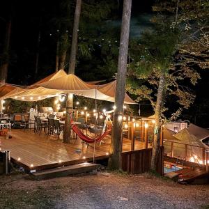 a tent with tables and chairs on a wooden deck at night at MUSIC FOREST Villa&Camp in Sasayama