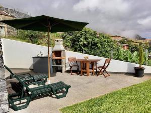a patio with a table and chairs and an umbrella at Refúgio de Pedra in Fajã da Ovelha