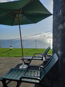 two lounge chairs with an umbrella on a patio at Refúgio de Pedra in Fajã da Ovelha