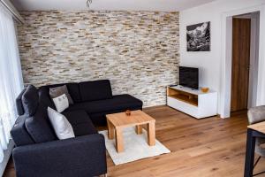 a living room with a black couch and a brick wall at Apartments Alpenfirn Saas-Fee in Saas-Fee