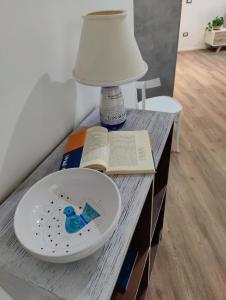 una mesa con una lámpara, una placa y un libro en Appartamento Maraviglios Alghero, en Alghero