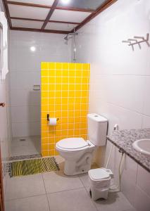 a bathroom with a toilet and a yellow tile wall at Pousada das Gaivotas in Guaibim