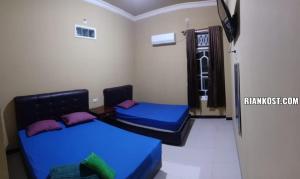 Duas camas num quarto com lençóis azuis e almofadas roxas em Rian Kost - Hotel Penginapan Murah Pusat Kota Palembang em Palimbão