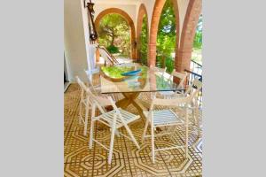 uma mesa de vidro com cadeiras brancas num pátio em Agradable casa de campo con piscina en la Barrosa em Chiclana de la Frontera