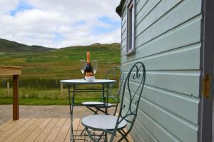 a table and chairs on a deck with a bottle of wine at Corriemuckloch Unique Huts in Dunkeld