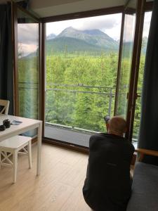 un homme assis sur une chaise devant une grande fenêtre dans l'établissement Apartment No.35, à Vysoke Tatry - Horny Smokovec