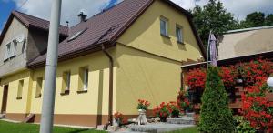 a yellow house with red flowers in a yard at Apartament "Rodzinny zakątek" in Duszniki Zdrój