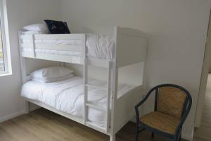 Cette chambre comprend un lit superposé blanc avec une chaise. dans l'établissement The Boat Shed, Westport, à Westport