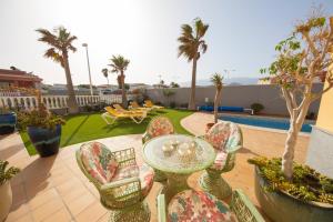 a patio with a glass table and chairs and palm trees at MEDANO4YOU Casa Girasol in El Médano