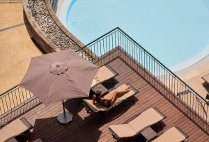 a woman sitting on a balcony with an umbrella at The Cliff Bay - PortoBay in Funchal