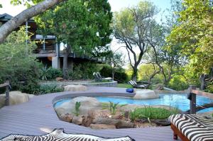 a swimming pool in a garden with trees and a building at Greenfire Game Lodge in Balule Game Reserve