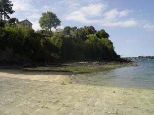 a beach with a house on a hill next to the water at OG Gîte in Le Minihic-sur-Rance