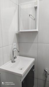 Baño blanco con lavabo y espejo en Pousada Quarto com tv,ar,frigobar,wifi e garagem, en Aparecida