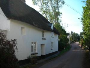 a white house with a thatched roof on a street at Splatthayes in Buckerell