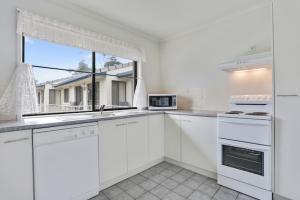 a white kitchen with white appliances and a window at Ocean Drive Apartments in Merimbula
