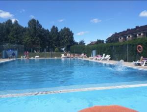 uma grande piscina azul com pessoas sentadas à sua volta em Los Sauces adosado a 10 minutos de Oviedo y 15 de Gijon em Llanera