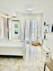 a white bedroom with a bed and a large window at Studio Crazy Beach Summerland in Mamaia