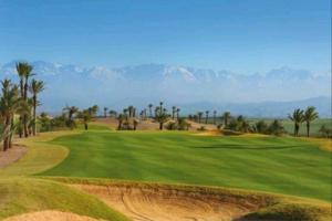 un campo de golf con palmeras y montañas al fondo en Cosy Loft Emeraude Marrakech Prestigia Golf City, en Marrakech