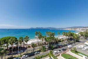 - une vue sur la plage bordée de palmiers et l'océan dans l'établissement Palais des Iles YourHostHelper, à Cannes