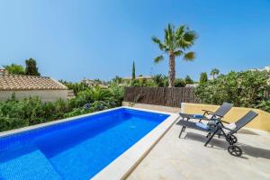 a villa with a swimming pool with two chairs and a palm tree at Casa Folara in Cala Llombards