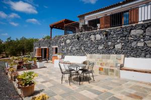 eine Terrasse mit einem Tisch und Stühlen vor einer Steinmauer in der Unterkunft Villa Las Rosas, Los Menores, Adeje, sea view in Armeñime