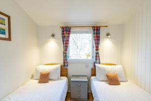 two beds in a small room with a window at Heather Lodge 12 with Hot Tub in Belladrum
