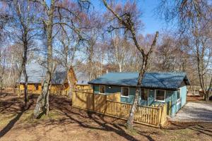 a house in the woods with a fence and trees at Heather Lodge 12 with Hot Tub in Belladrum