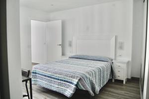 a white bedroom with a bed with a striped blanket at Apartamento Loft Lucena in Lucena