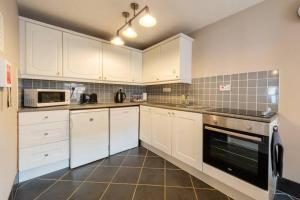 a kitchen with white cabinets and a stove top oven at 2 Mews Cottages - Town Centre Location in Appleby