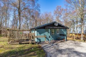 a small green building with a fence in a field at Fern Lodge 11 with Hot Tub in Belladrum