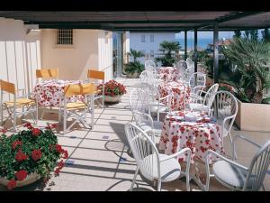 un patio con mesas blancas, sillas blancas y flores en Hotel Emma Nord en Rímini