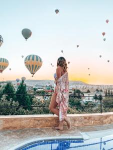 una chica parada en una cornisa mirando globos de aire caliente en Cappadocia Caves Hotel en Göreme