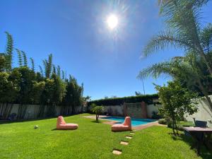 a backyard with a pool with red chairs in the grass at Lilas Park Villa - Casablanca Bouskoura in Casablanca
