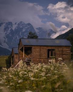 eine Holzhütte auf einem Feld mit Bergen im Hintergrund in der Unterkunft Ushguli Cabins in Uschguli