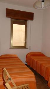 two beds in a room with a window and a chair at Appartamento fronte mare San vito lo capo in San Vito lo Capo