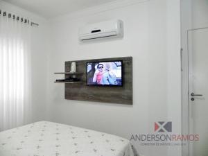1 dormitorio con TV en una pared blanca en 1056 - Apartamento para locação na praia de Bombinhas, en Bombinhas
